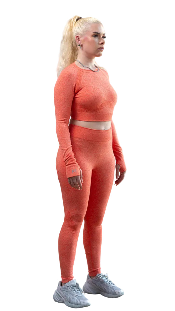 Person wearing an orange athletic outfit standing on a wooden floor with a white wall background